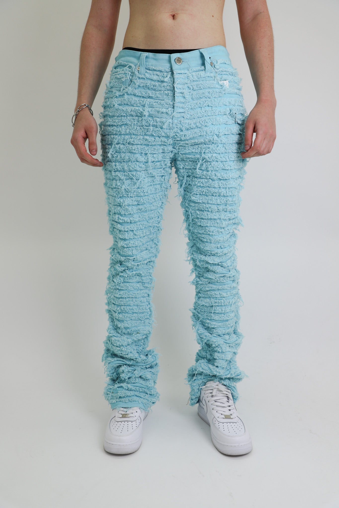 Front view of light blue frayed stacked jeans with five pockets.