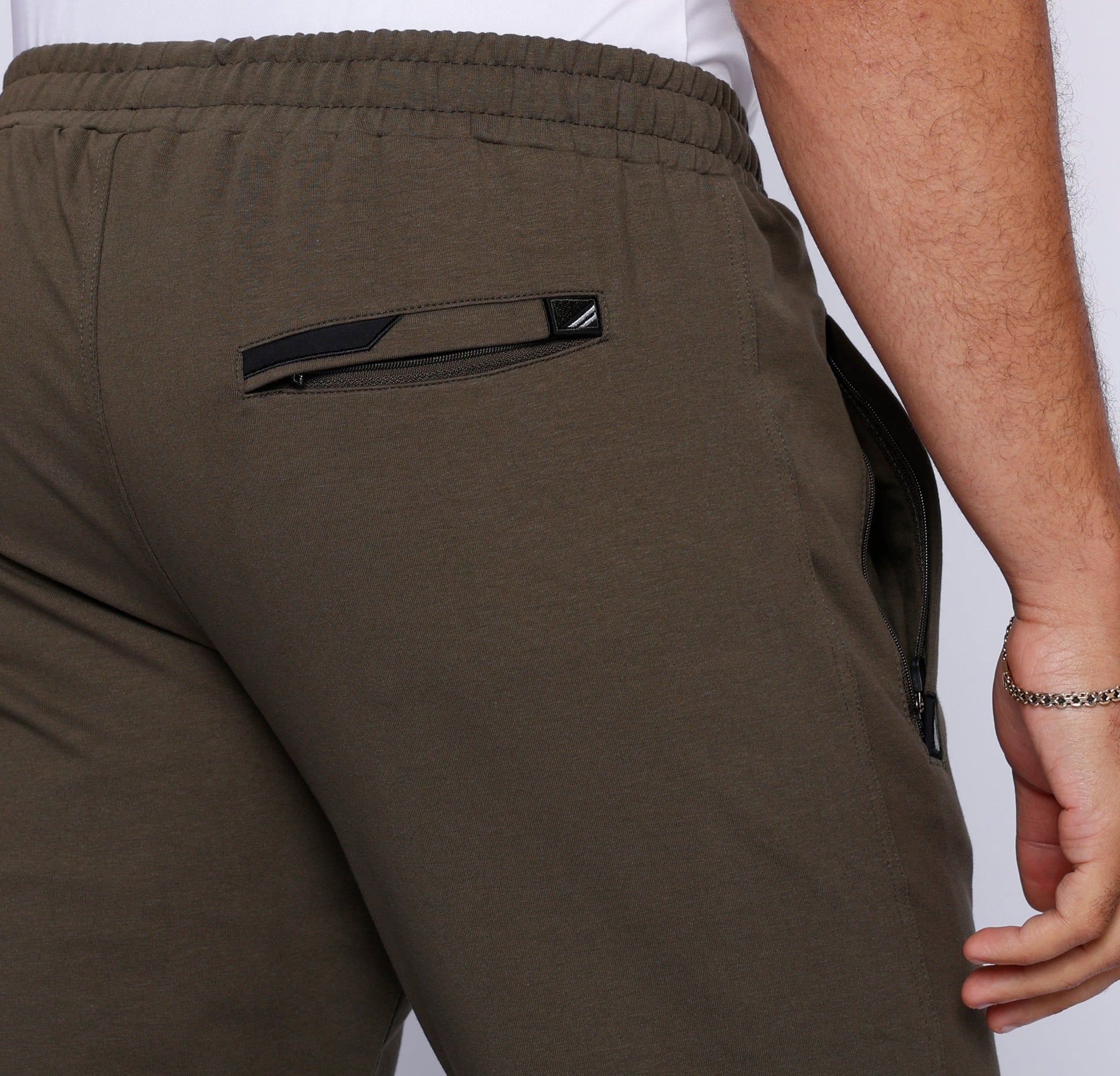 Detail shot of dark khaki athletic pants showing back pocket and elastic waistband.