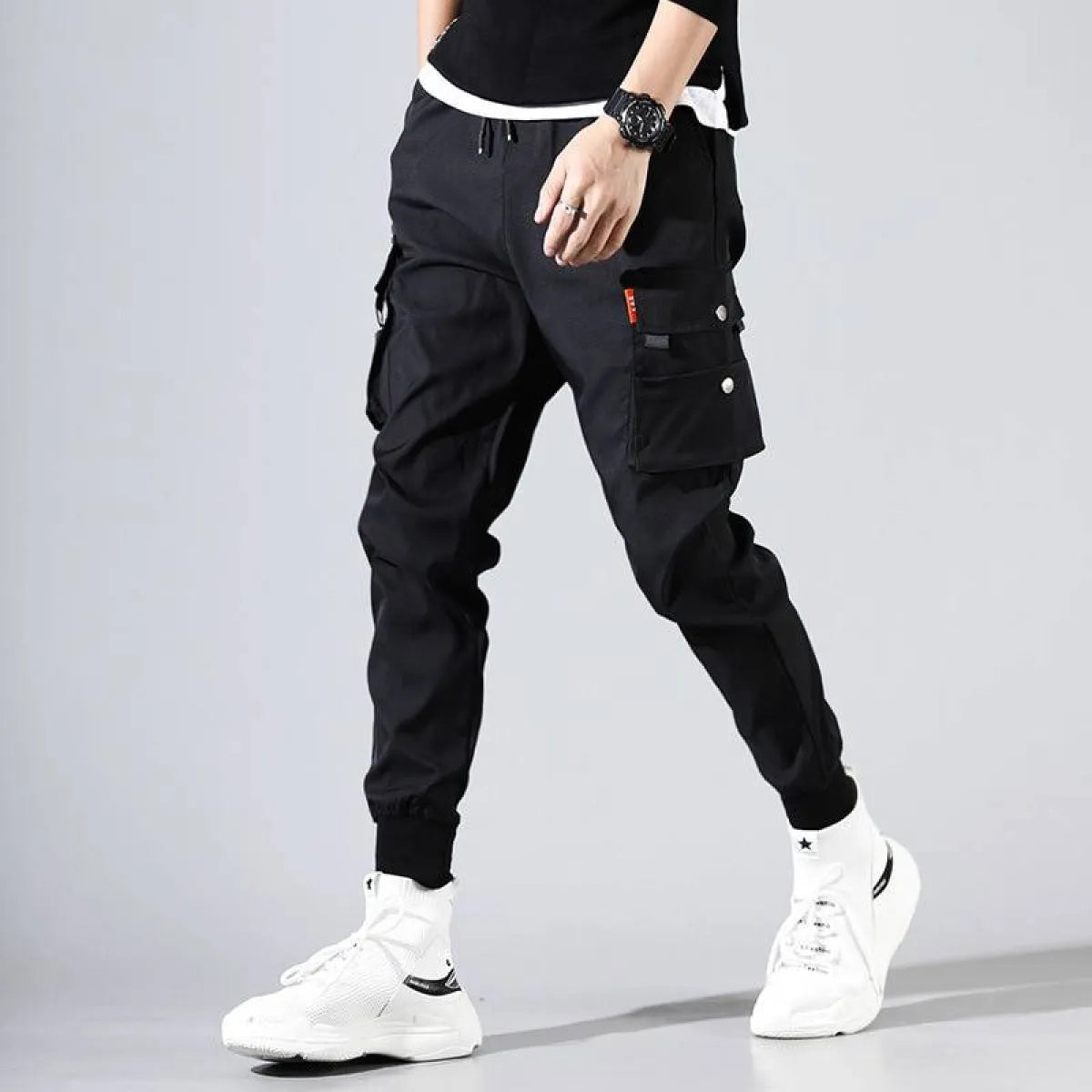Lifestyle shot of black Harajuku men's pants with cargo pockets and tapered fit.