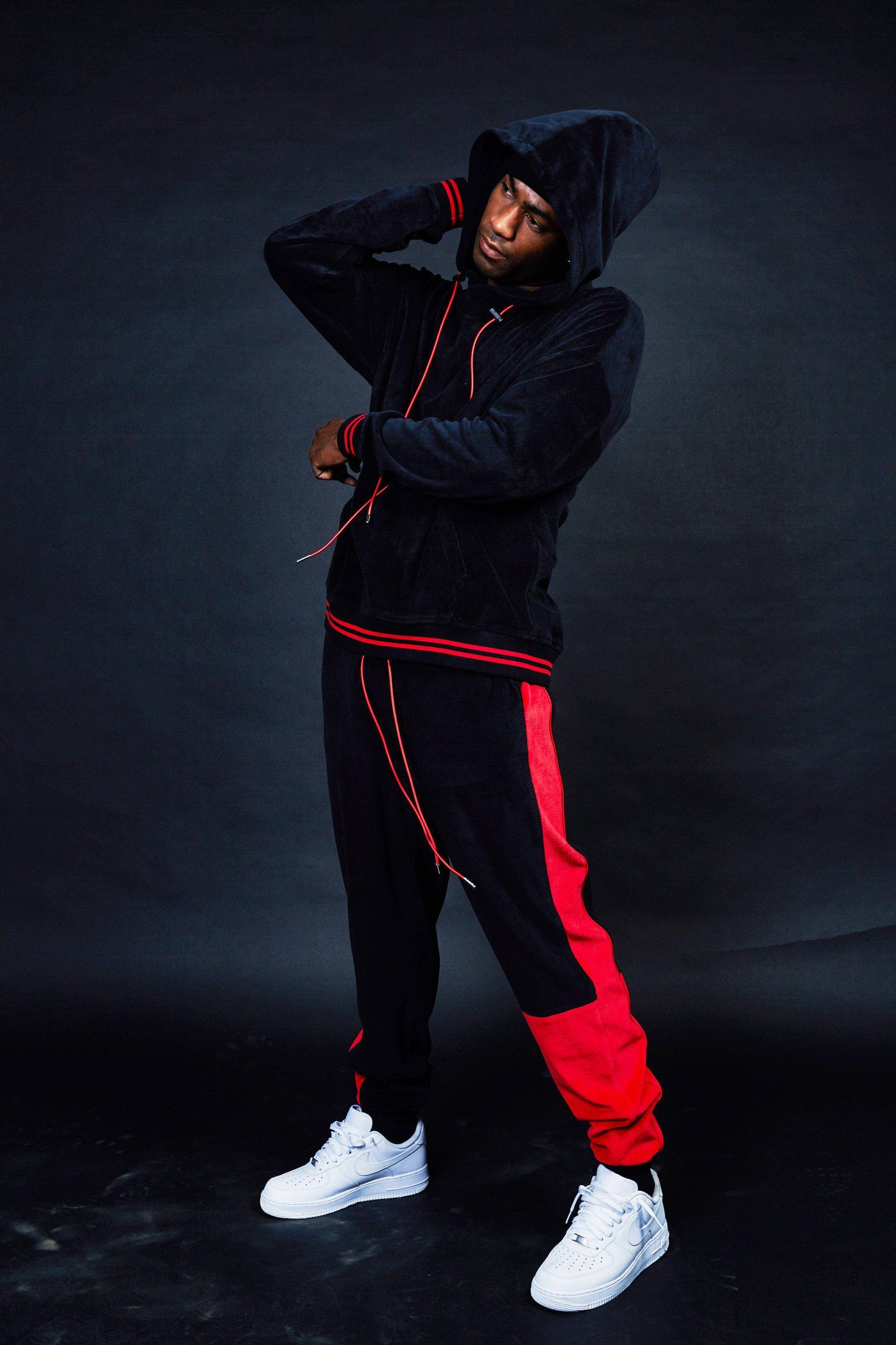 Lifestyle shot of black tracksuit with red stripes in a studio setting.