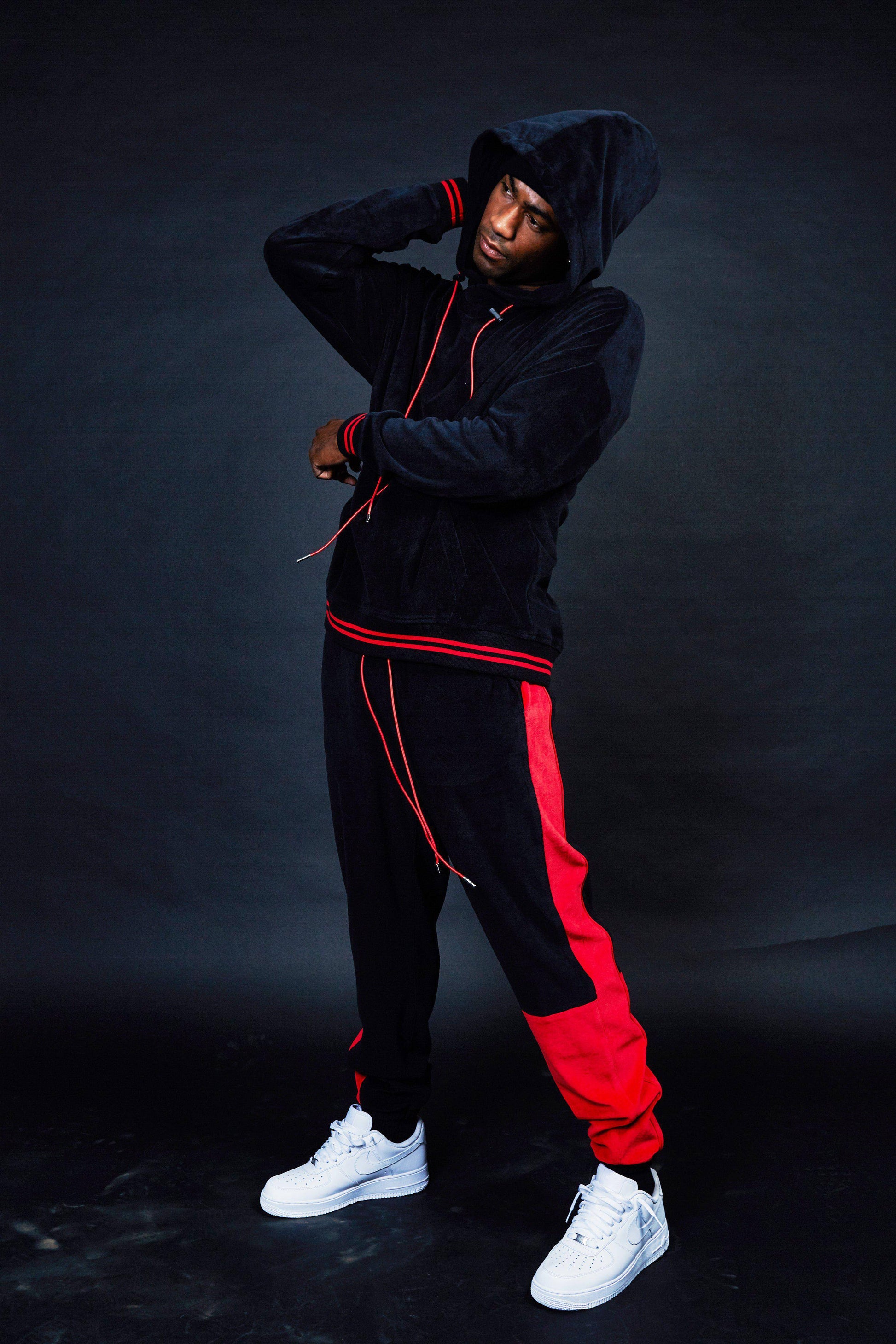 Lifestyle shot of black tracksuit with red stripes in a studio setting.