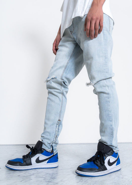 Light blue jeans with ripped knees in a lifestyle shot against a white background