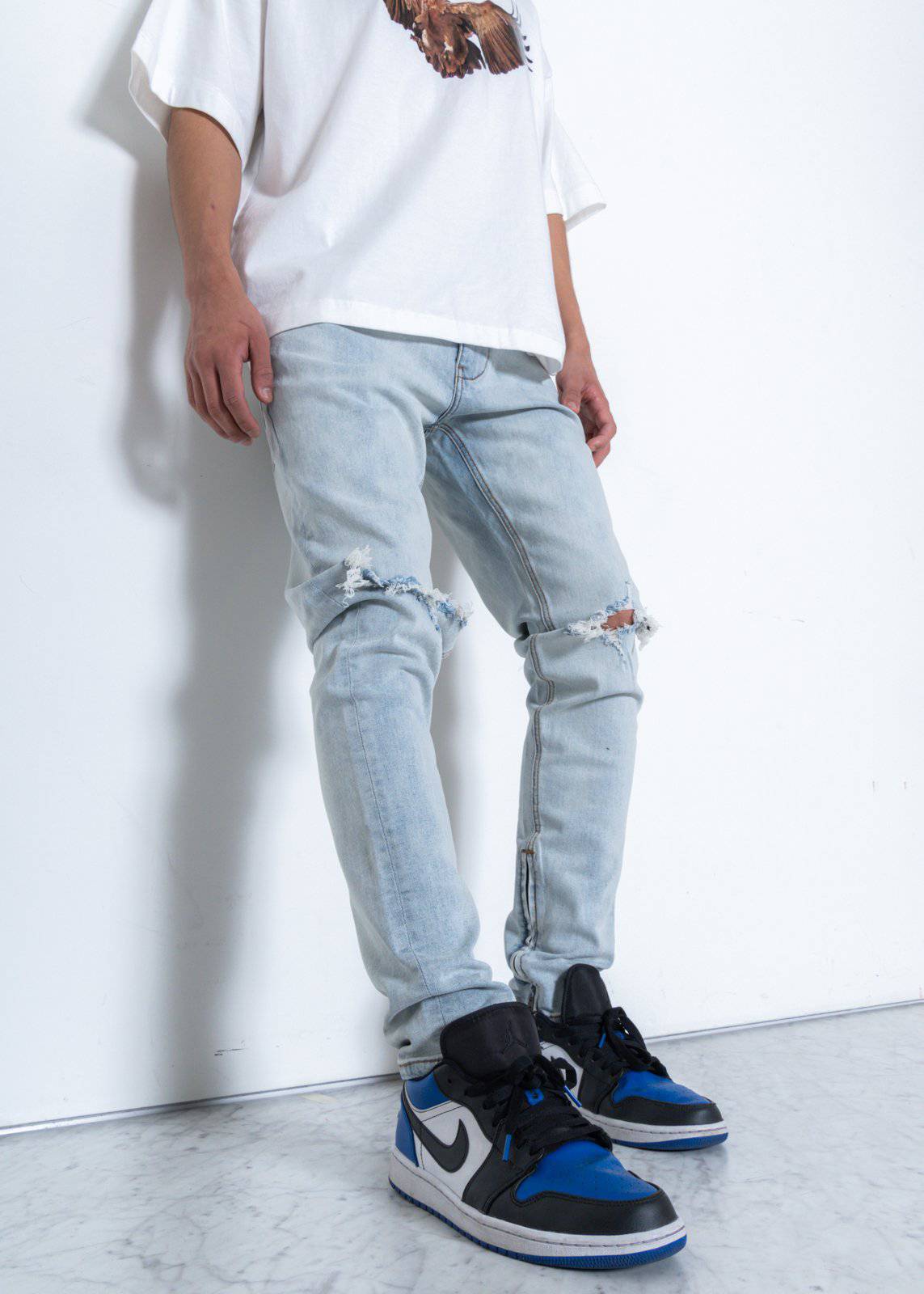 Lifestyle shot of light blue jeans featuring ripped knees on a white background