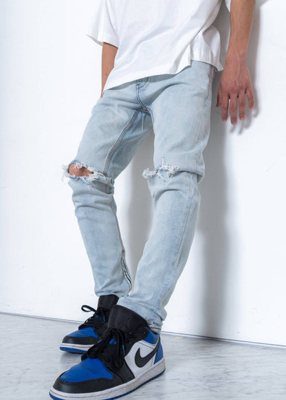 Lifestyle view of light blue jeans with a slim fit and ripped knees against a white background