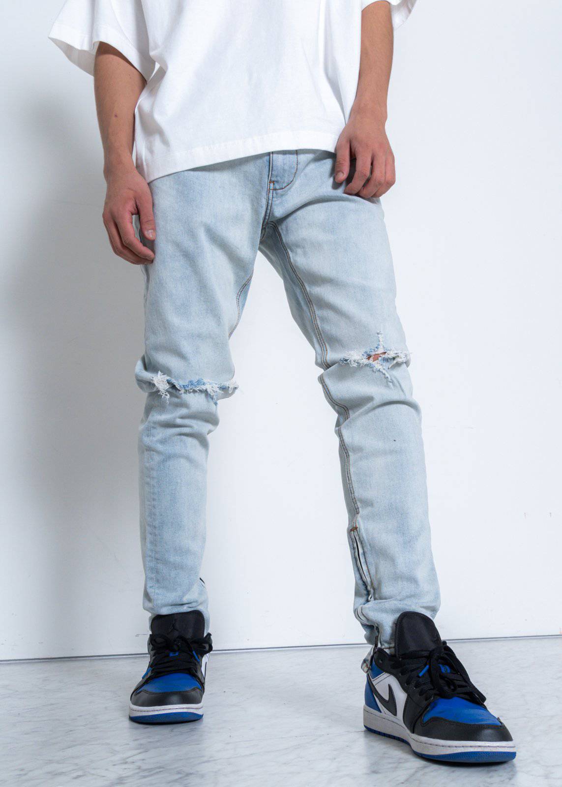 Lifestyle image of light blue jeans showcasing ripped knees on a white background