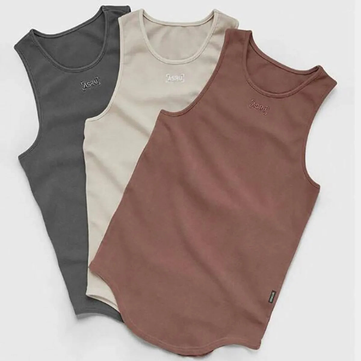 Lifestyle shot of three tank tops in black, beige, and brown showcasing sleeveless style.