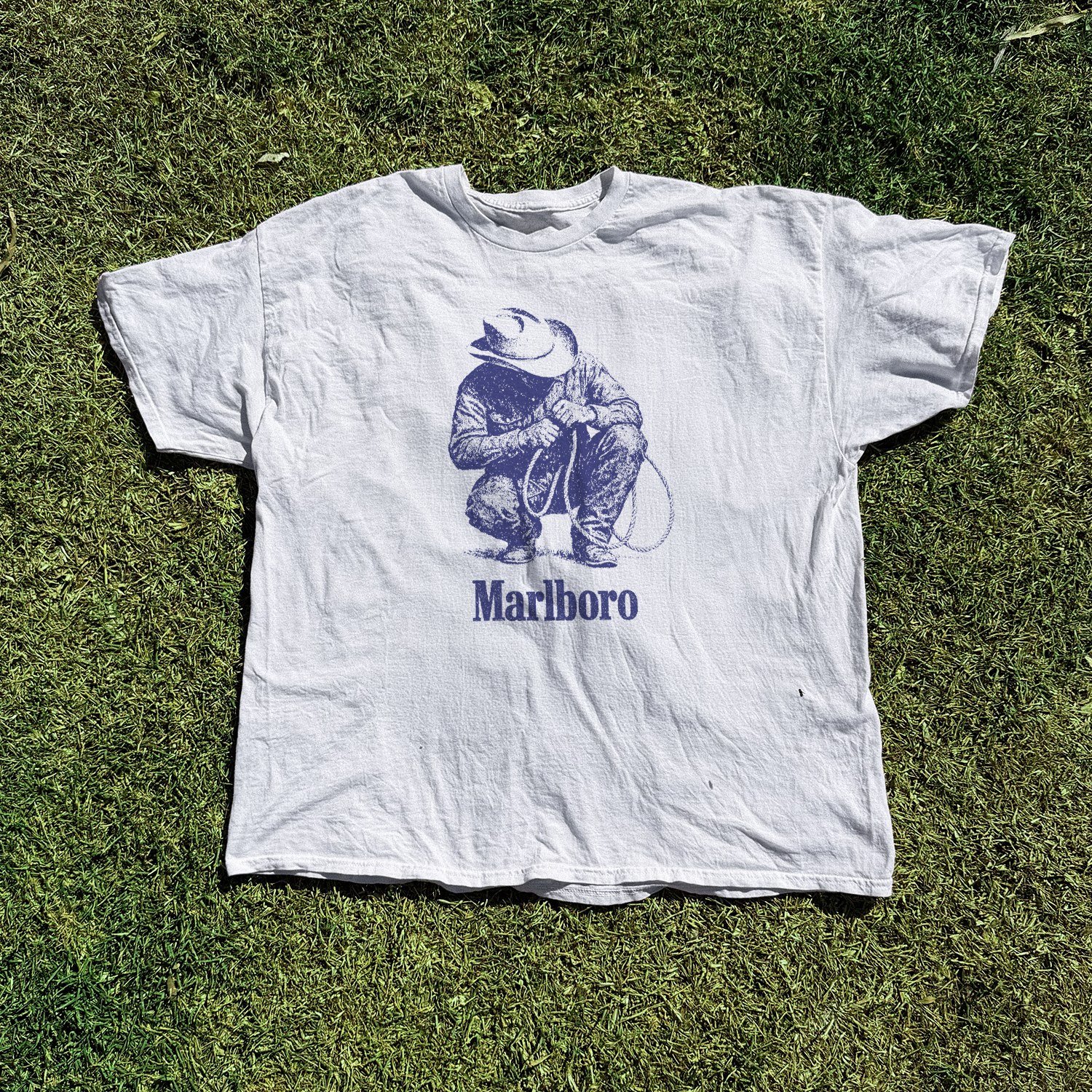 Graphic white t-shirt laid flat on grass.